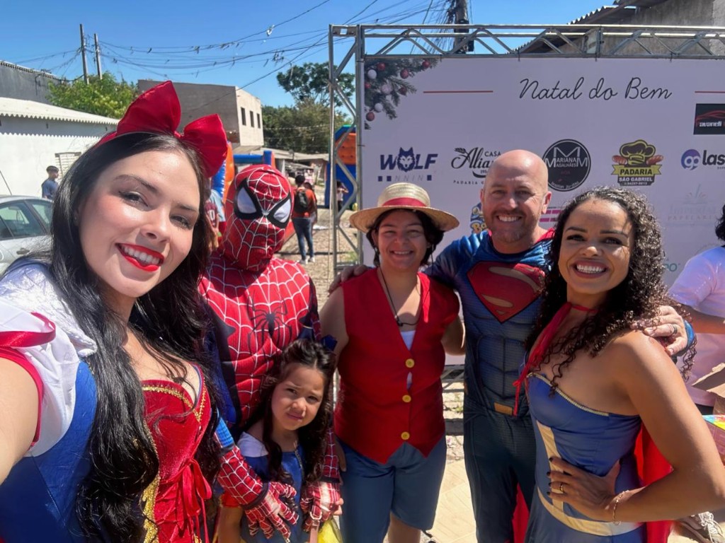 Grupo de voluntários fantasiados em evento solidário com painel de apoiadores